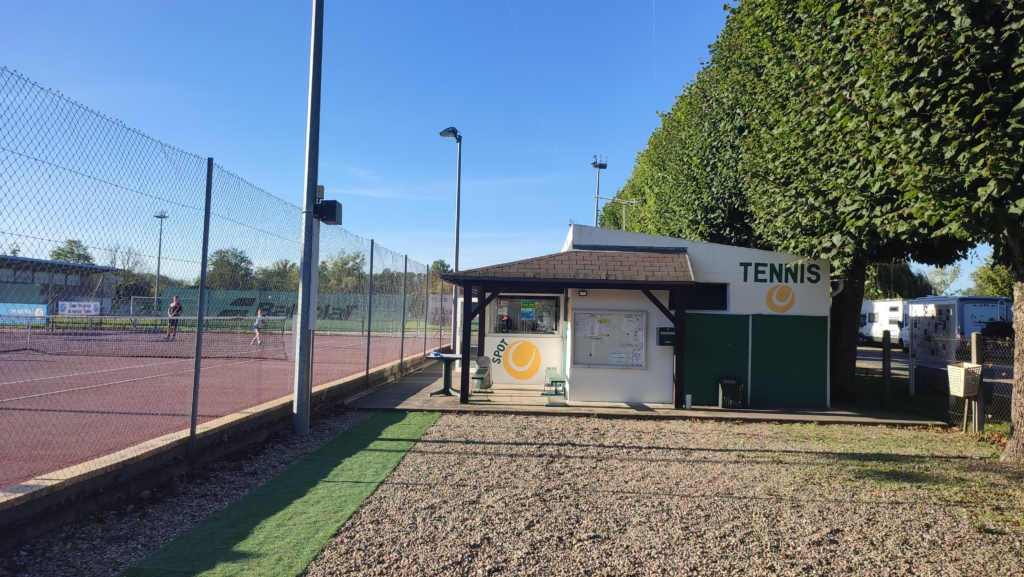 Court de tennis sur la droite de l'image occupé par des enfants avec à gauche les logos du spot le club local