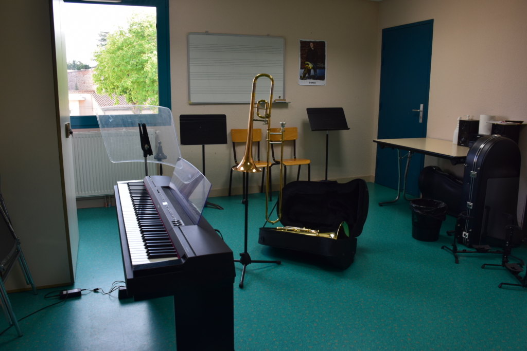 Salle de musique avec un piano, un saxophone et un trombone rangé dans sa malette