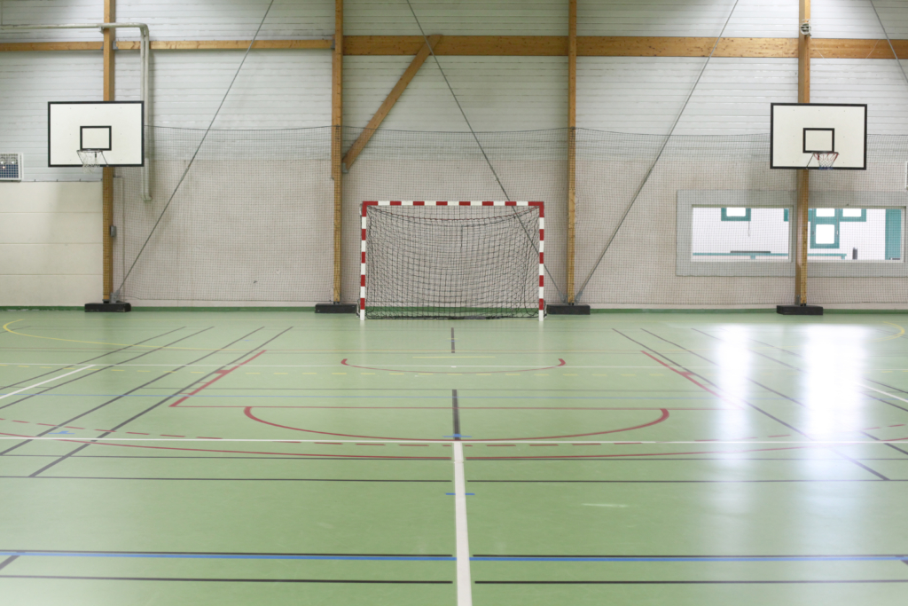 Parquet de la salle Jean Reynaud avec but de handball et paniers de basket apparents