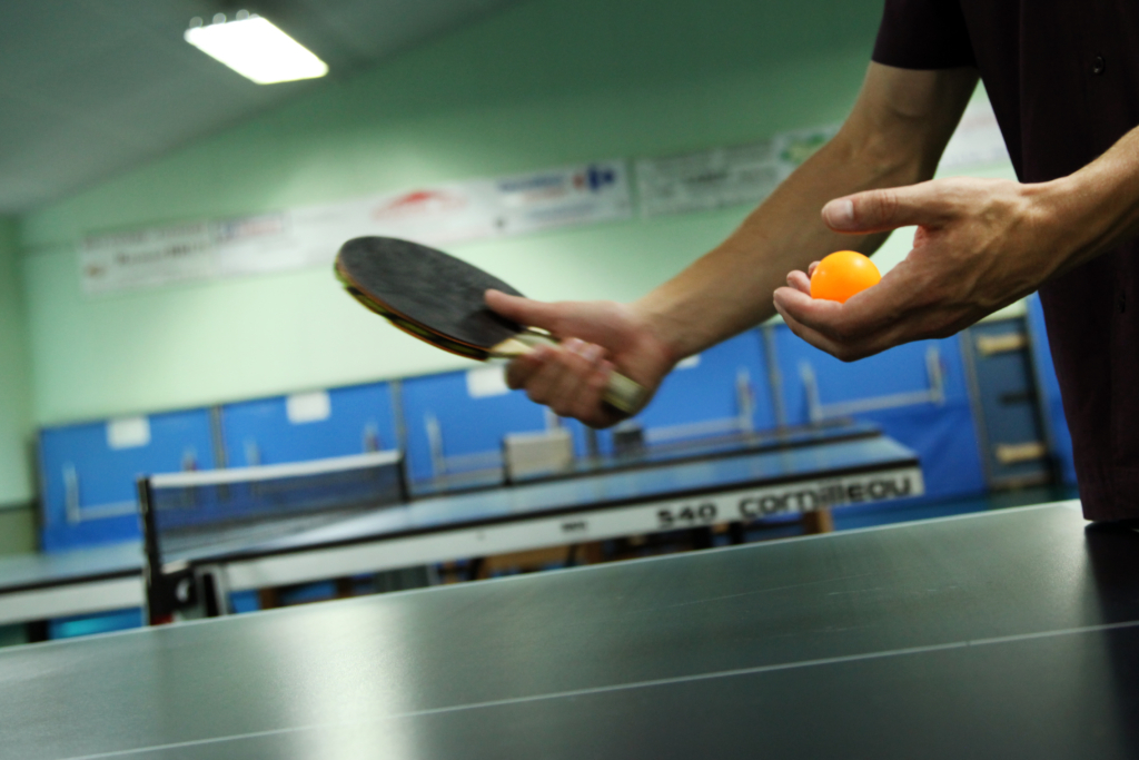 Partie d'un joueur en train de servir face à la table de tennis de table